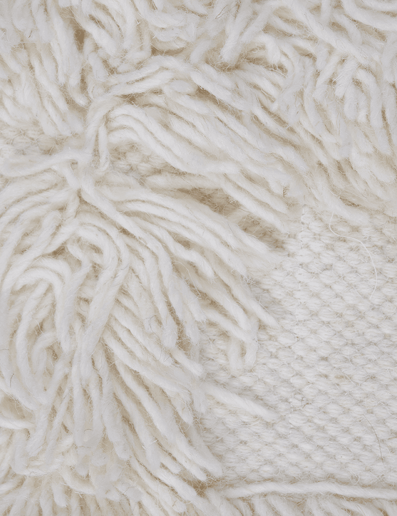 Detaljbild av Rio väggbonad i off-white handvävd ull som visar tuftat mönster och vävd botten.