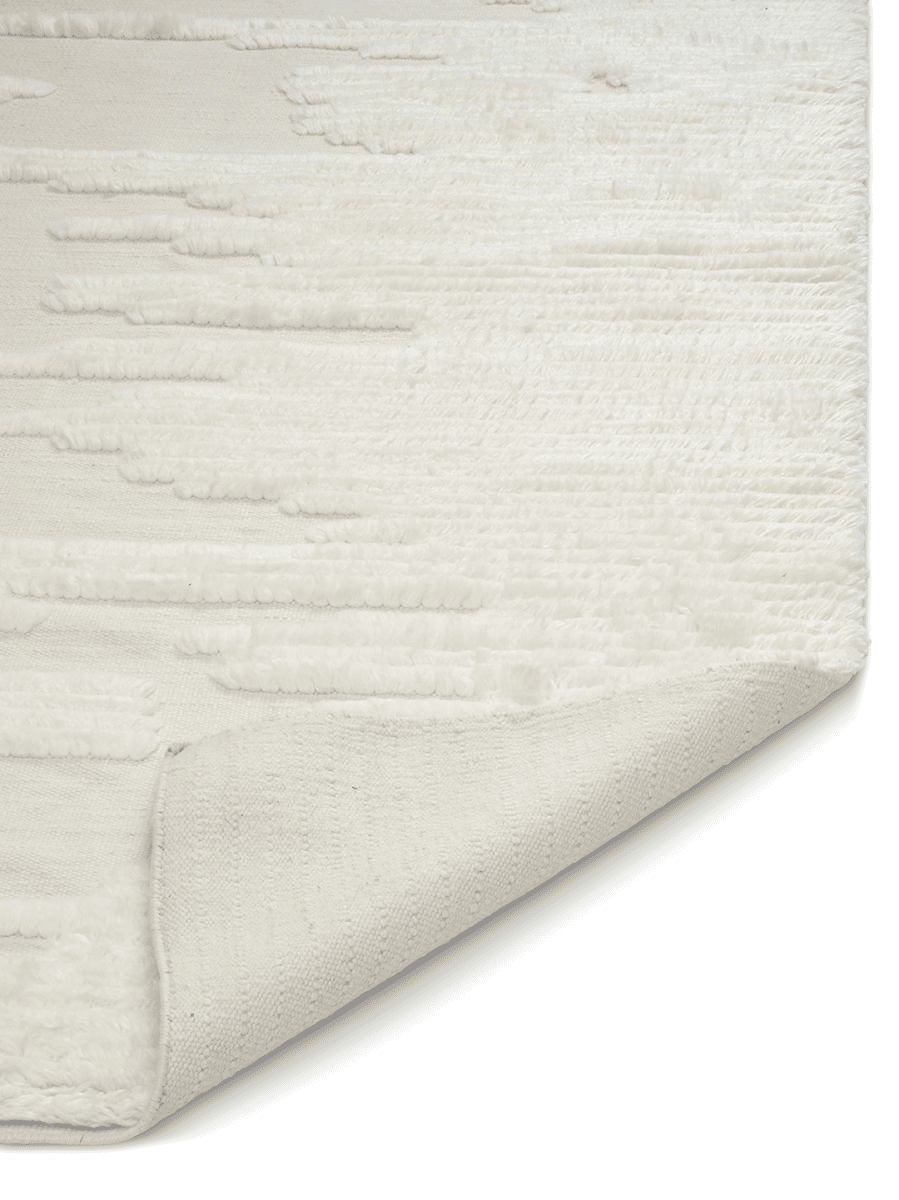 Cream textured area rug with a tufted abstract pattern and a folded corner showing the woven cotton backing.