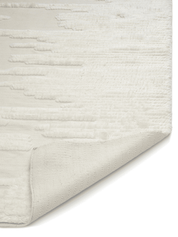 Cream textured area rug with a tufted abstract pattern and a folded corner showing the woven cotton backing.