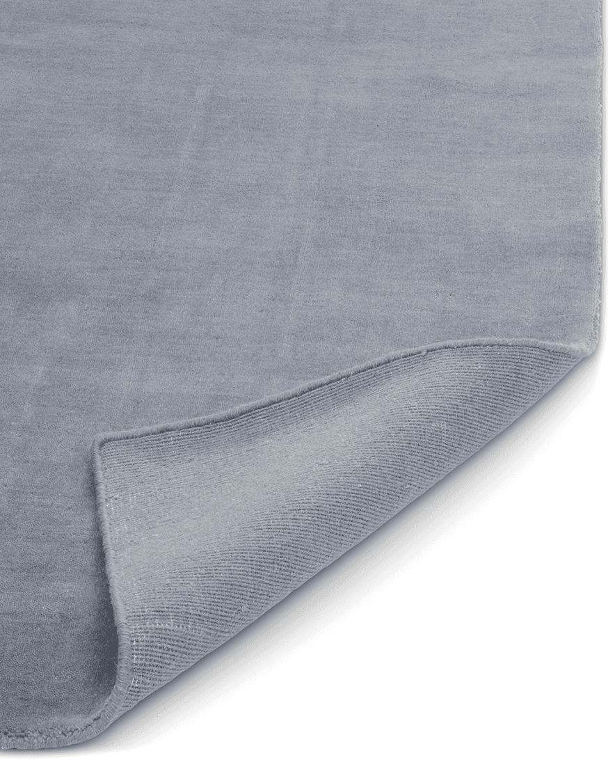 Frilagd bild av handvävd ullmatta Solid Blå, rektangulär med kort lugg och diskret lyster. Detaljbild med ett uppvikt hörn.