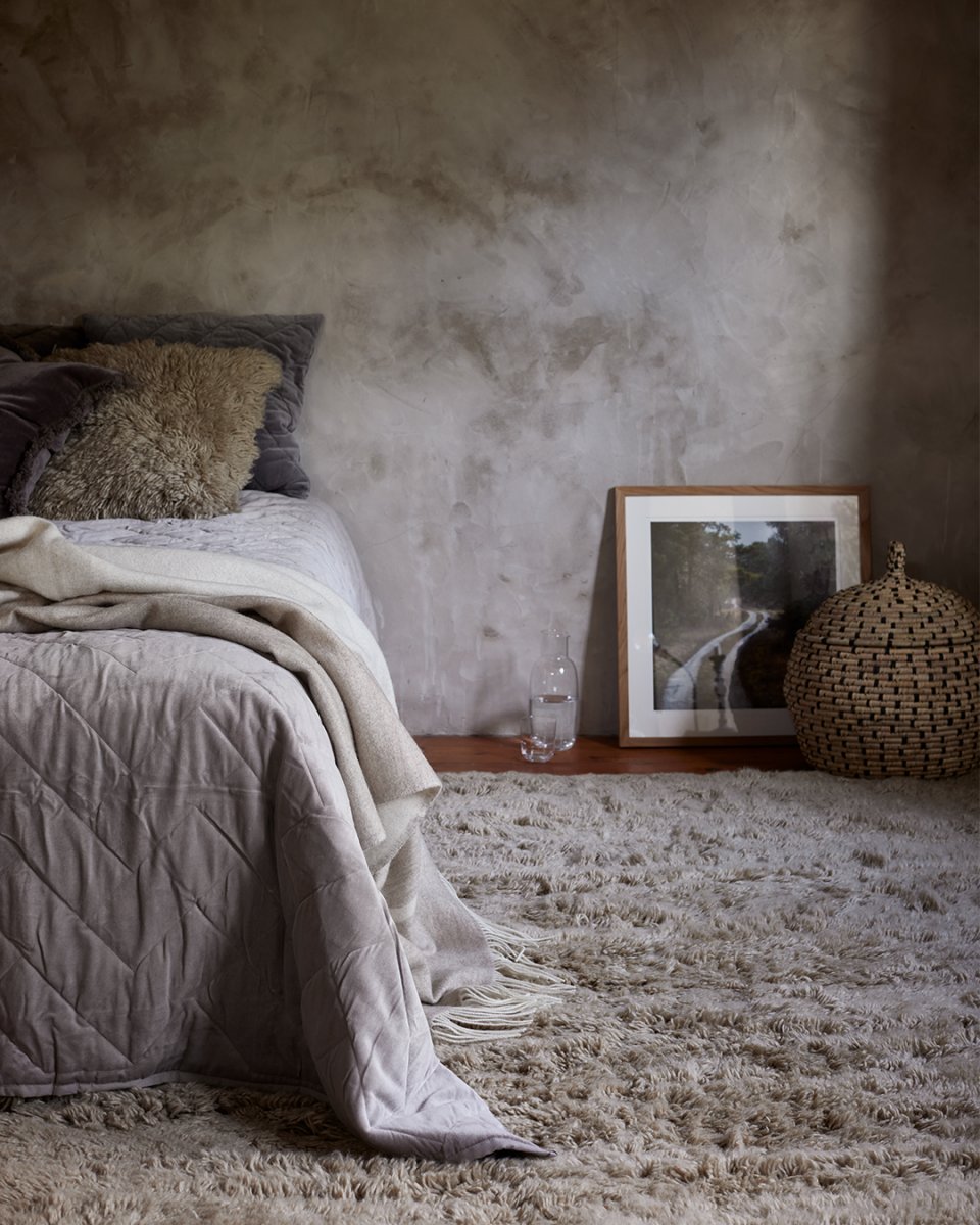 Cozy bedroom interior featuring a textured beige shag rug, quilted bedding, and a decorative woven basket.