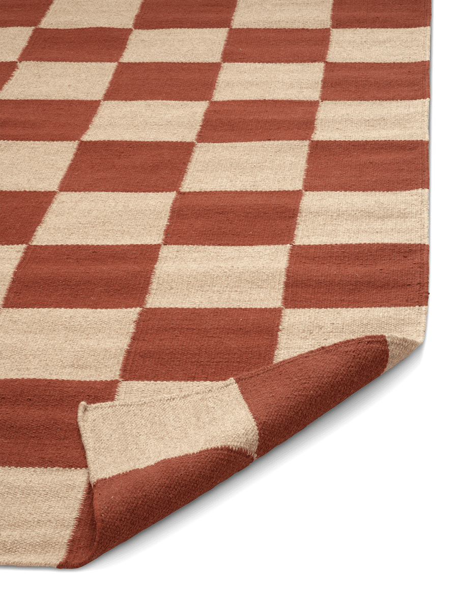 Wollteppich mit rot-beigem Schachbrettmuster und umgeschlagener Ecke im modernen Design.