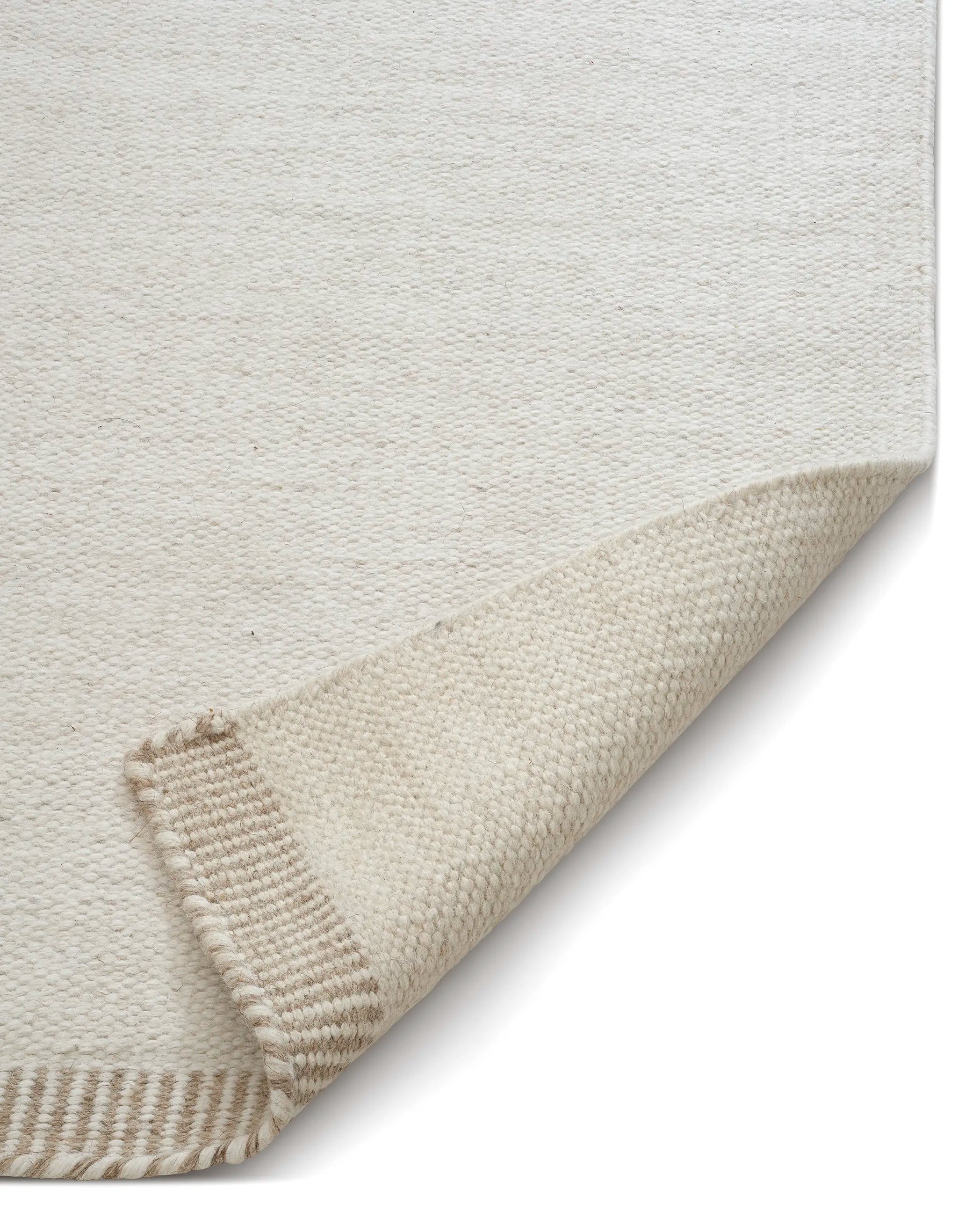 Close-up of a cream-colored woven wool area rug with a folded corner revealing a beige textured underside.