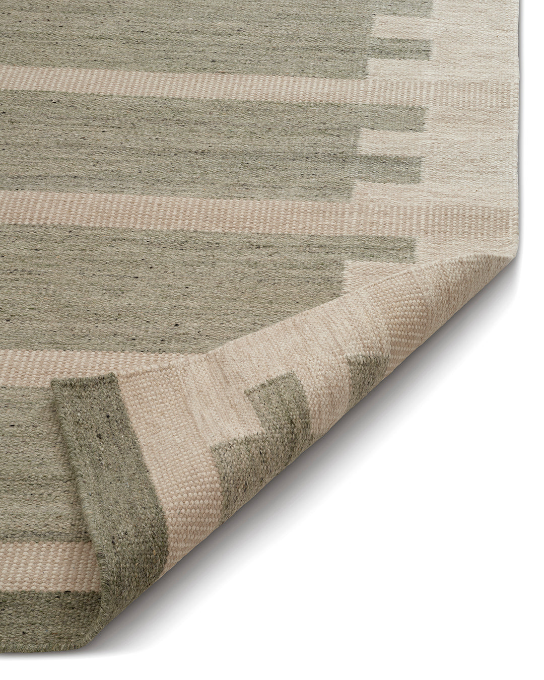 Vävd matta i ull med geometriskt mönster i gröna och beige nyanser, visad med ett uppvikt hörn för att visa texturen.