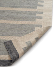 Vävd ullmatta i grå och beige med geometriskt mönster och invikt hörn.