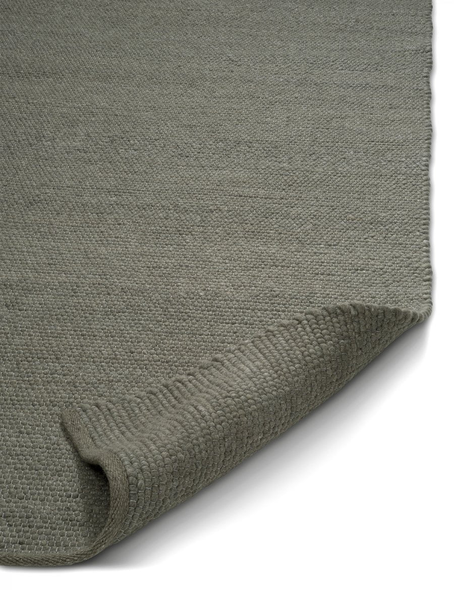 Sage green textured wool area rug with a folded corner showing the dense, woven loop construction.
