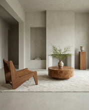 Modernt vardagsrum med rund soffbord i valnötsträ, en stilren fåtölj och en mönstrad beige matta i minimalistisk stil.