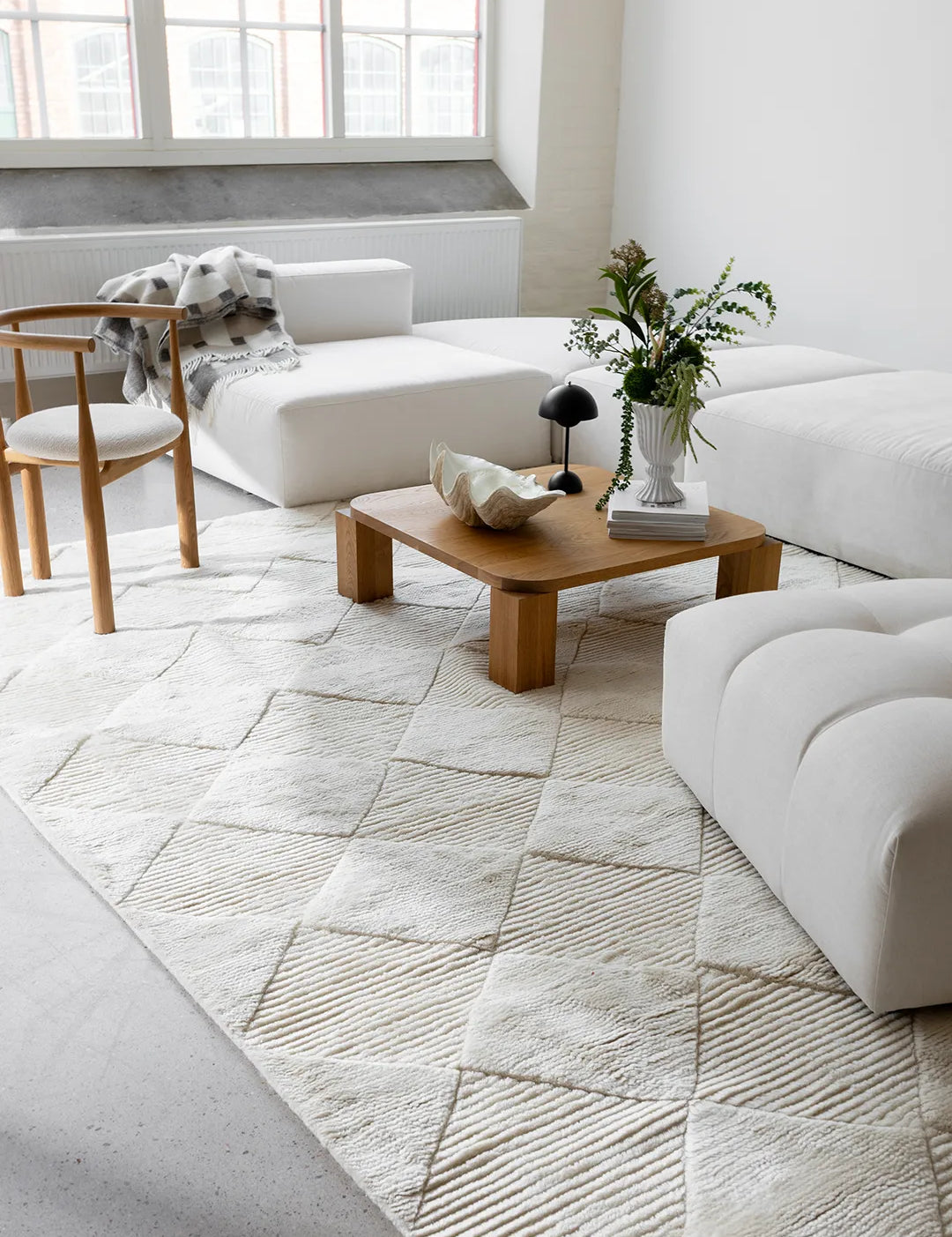 Matta Berber Ivory, handvävd i vit ull med diskret rutmönster, placerad i ljust vardagsrum med soffor och träbord.