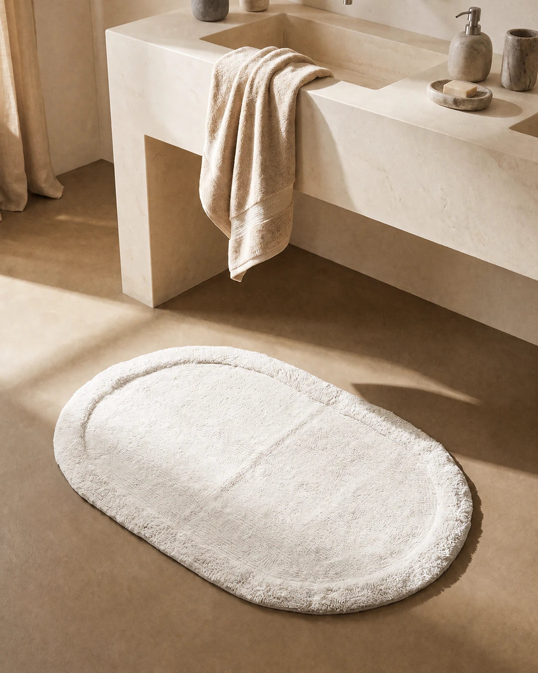 Vit oval badrumsmatta Border Oval från Classic Collection, 60x90 cm i bomull, placerad framför ett ljust handfat i ett varmt neutralt badrum.