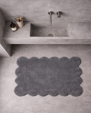 Badrumsmatta Clam i grå bomull placerad framför handfat i badrum med stenytor och väggmonterad tvättställslösning