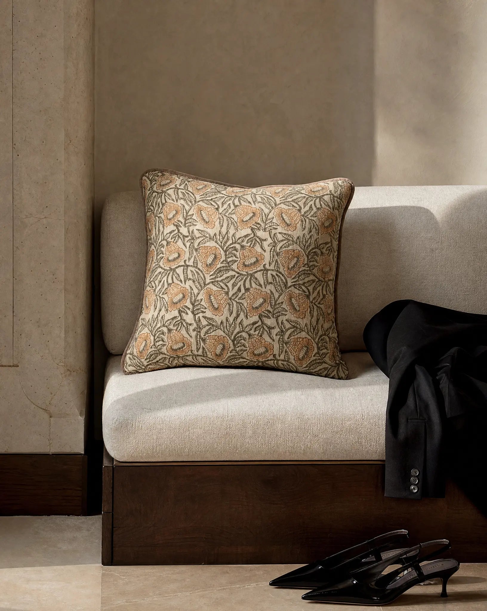 Kuddfodral Bell Gul 50x50 cm från Classic Collection med botaniskt blommönster i dämpade gula och gröngrå toner samt kontrasterande kantband, stylat på en ljus bänk i en elegant, neutral interiör.