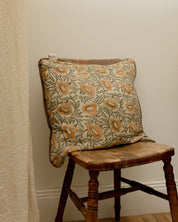Kuddfodral Bell Yellow i handtryckt bomull med blommönster och pipingkant, placerat på en trästol i hemmiljö.