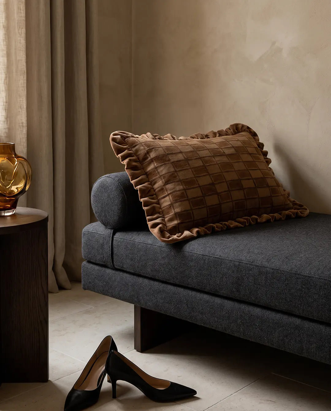 Kuddfodral Block Amber 40x60 cm från Classic Collection med rutigt mönster och dekorativ volang, stylat på en mörkgrå soffa i en varm, elegant interiör.