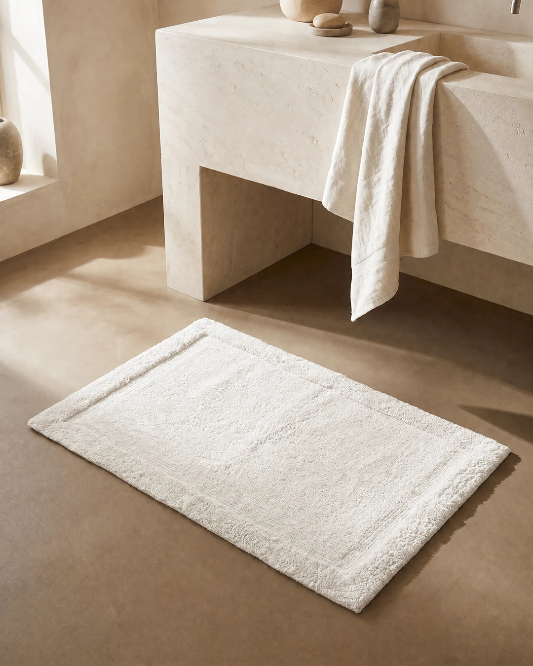 Badrumsmatta Border Vit från Classic Collection, 60x90 cm i bomull, placerad framför ett ljust handfat i ett varmt neutralt badrum.