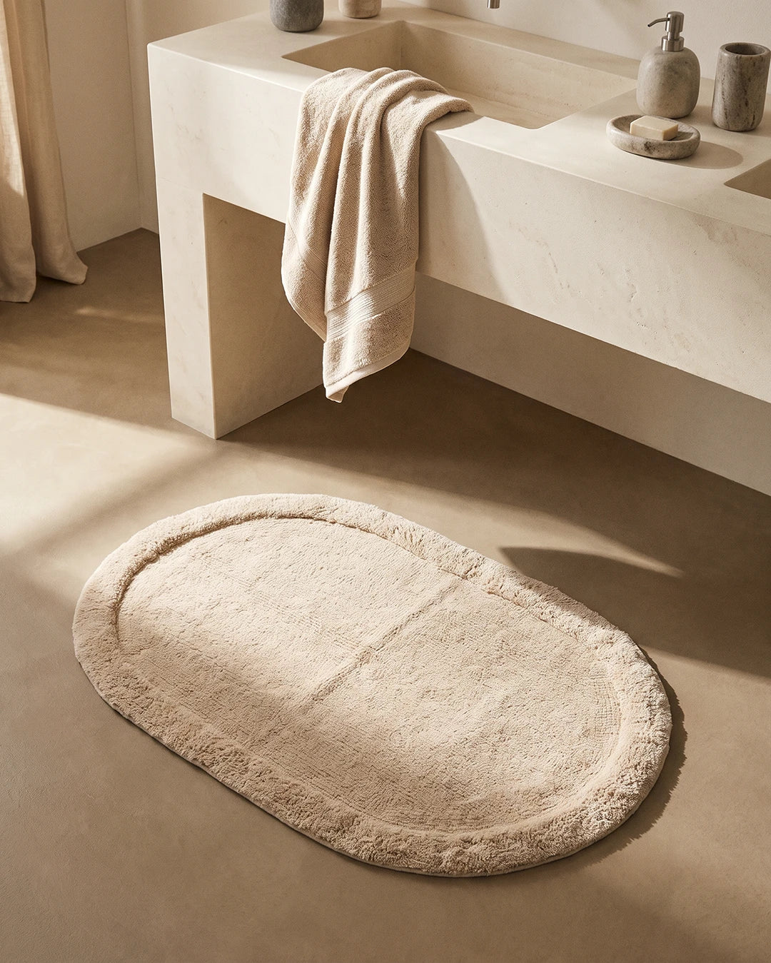 Badrumsmatta Border Oval Beige från Classic Collection, 60x90 cm i bomull, placerad framför ett ljust handfat i ett varmt neutralt badrum.