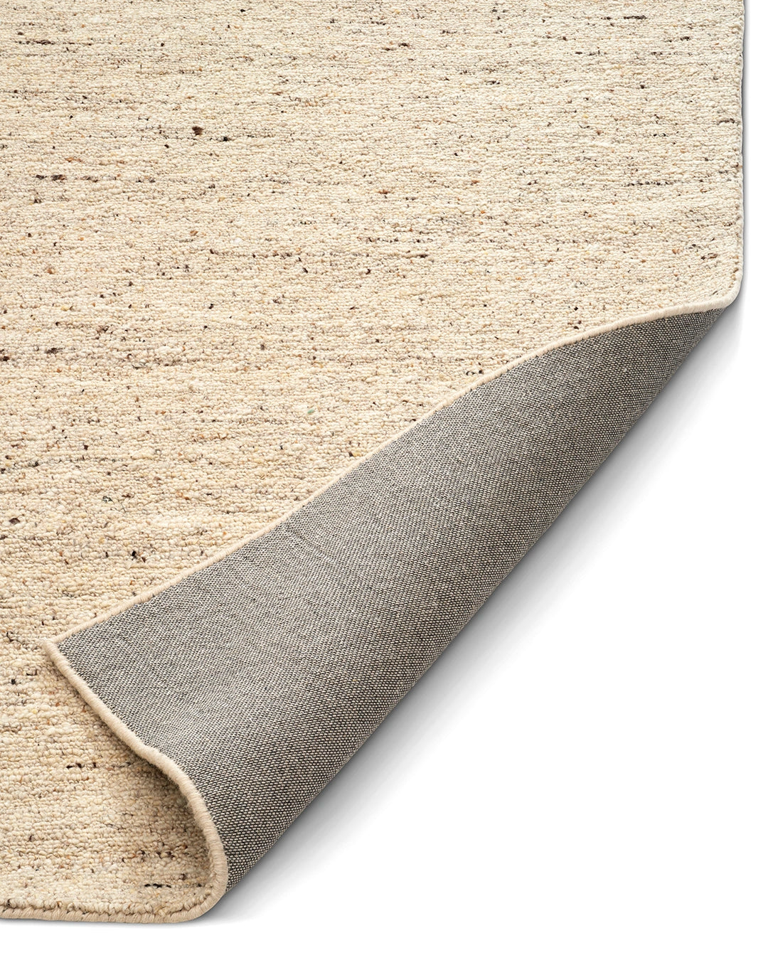 Närbild av Bouclé-matta i ljus beige ton med mörk melering och uppvikt hörn som visar den vävda baksidan.