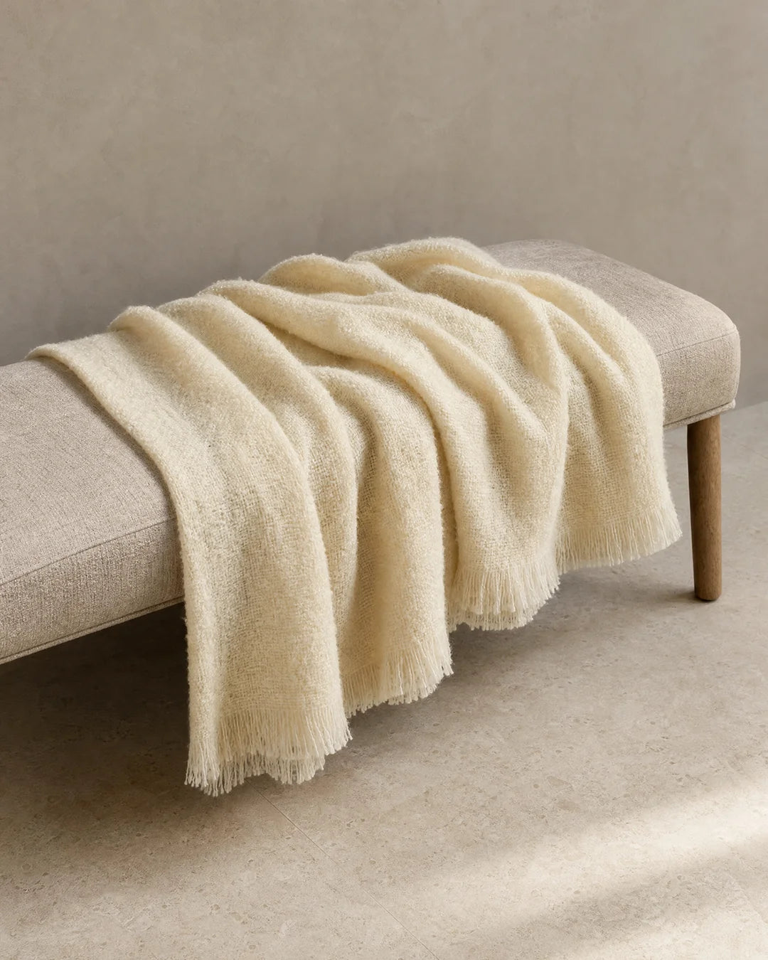 Pläd Bouclé Cream från Classic Collection i mjuk, strukturerad kvalitet med fransar, draperad över en ljus bänk.