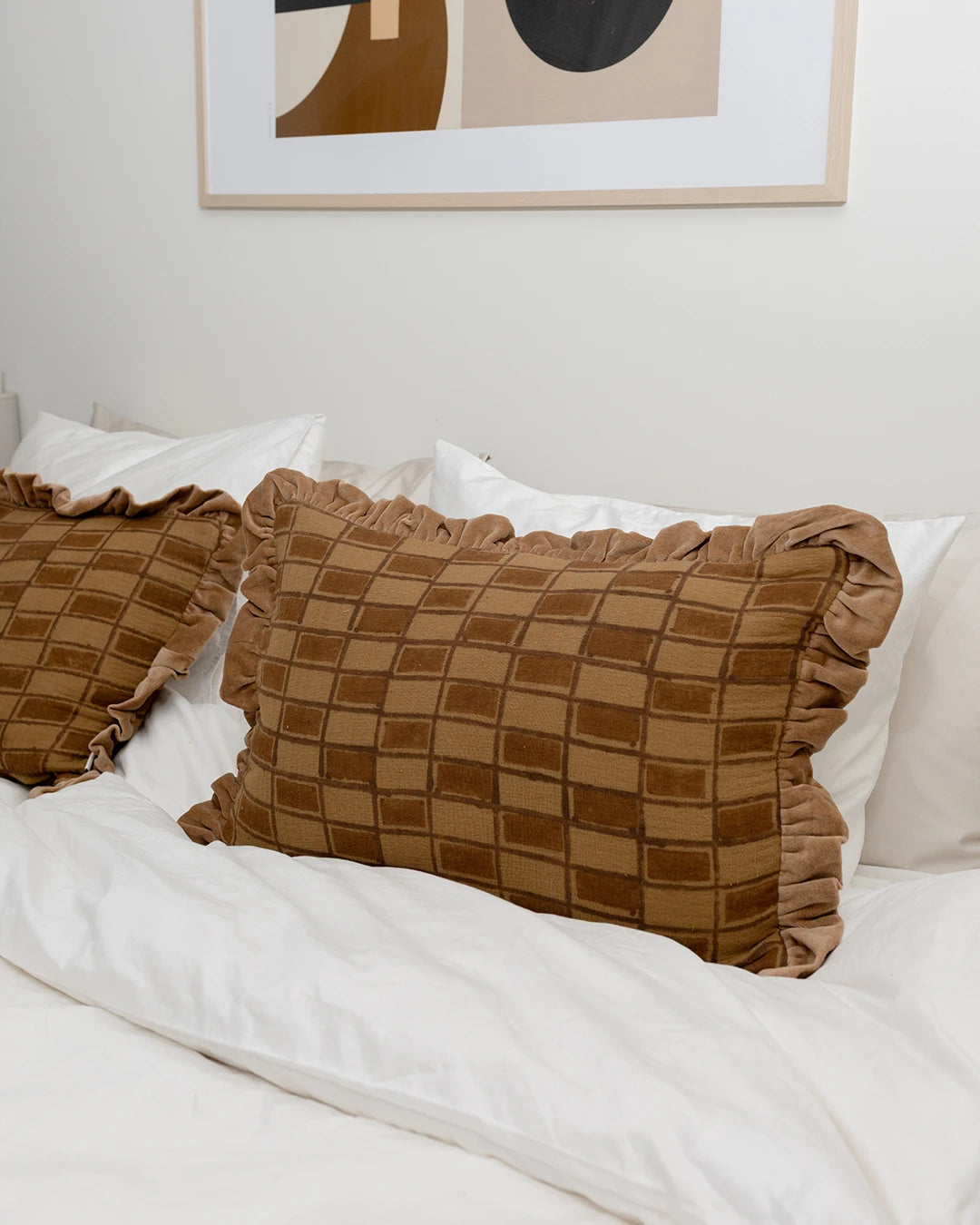 Handgjort kuddfodral i modellen Block Amber, tillverkat i bomull med blockprint-mönster. Kuddfodralet ligger på en bäddad säng tillsammans med vita sängkläder.