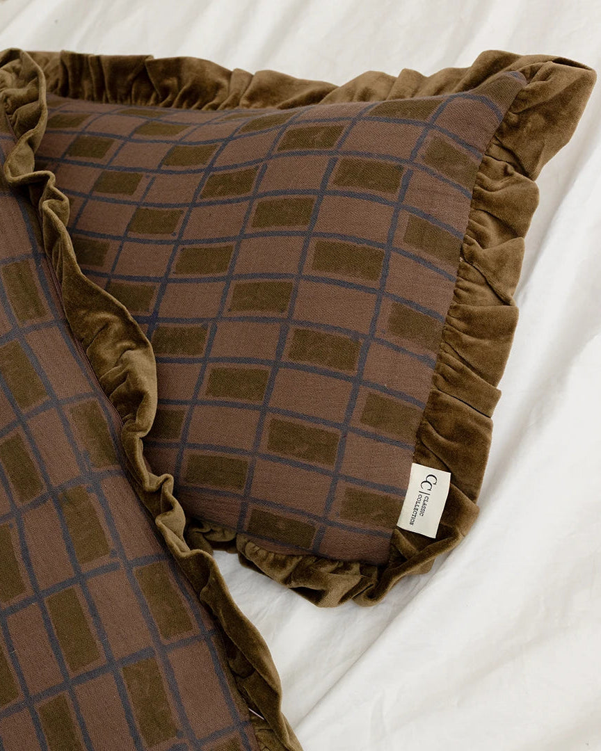 Handgjort kuddfodral Block Aubergine i bomull med blockprint-mönster och volangkant, placerat på en bäddad säng tillsammans med ett likadant kuddfodral.