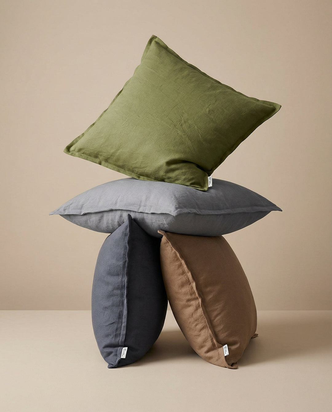 Stapel av fyrkantiga kuddar i linne i nyanser av olivgrönt, grått, mörkgrått och brunt.