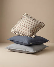 Stack of three linen throw pillows featuring a floral patterned ruffled cushion atop navy and grey solid square pillows.