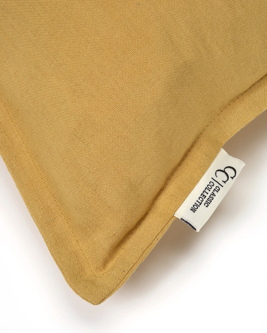 Gul prydnadskudde i linnematerial med Classic Collection-etikett och detaljerade sömmar.