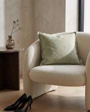 Kuddfodral Classic Linen Sage 50x50 cm från Classic Collection i enfärgat linne, stylat i en ljus fåtölj i en varm, neutral interiör.