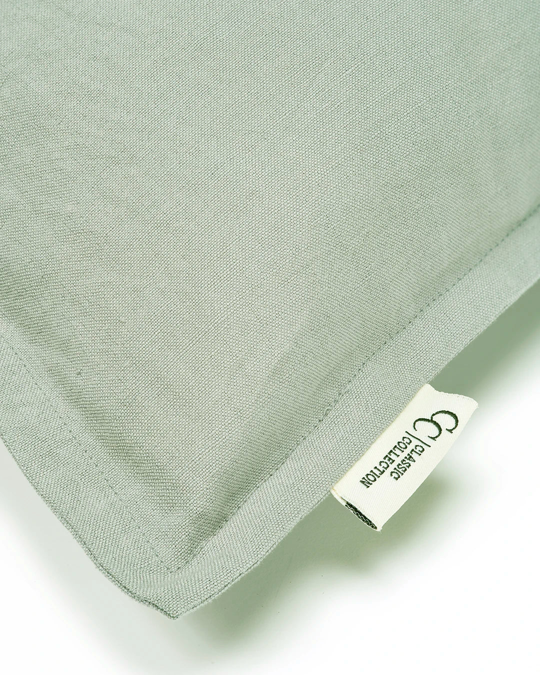 Close-up of a sage green linen throw pillow with a flange edge and a Classic Collection brand label.