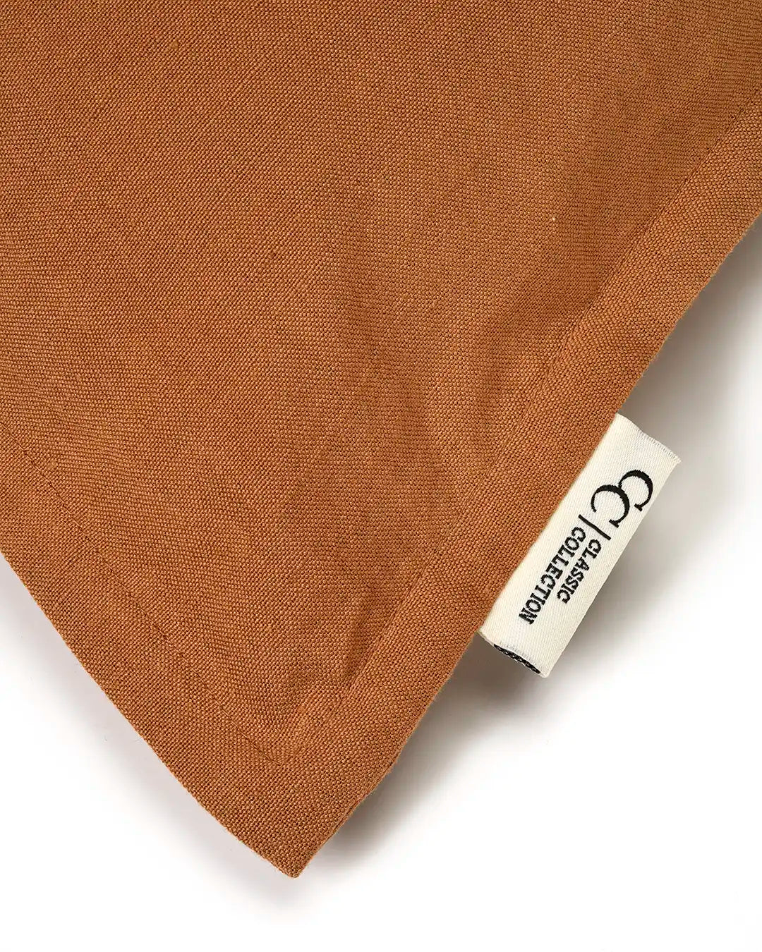 Närbild på ett rostrött kuddfodral i vävt tyg med en vit Classic Collection-etikett i hörnet.