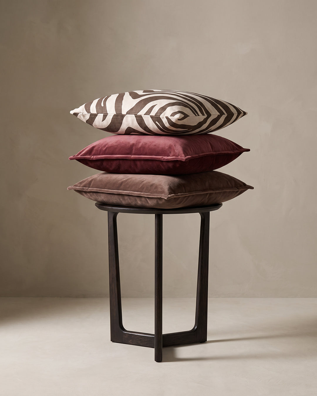 Kuddar 50x50 cm från Classic Collection: Savannah i off-white och brun samt Classic Velvet i burgundy och brun, arrangerade på ett mörkt sidobord.