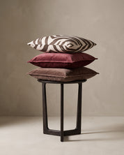 Kuddar 50x50 cm från Classic Collection: Savannah i off-white och brun samt Classic Velvet i burgundy och brun, arrangerade på ett mörkt sidobord.