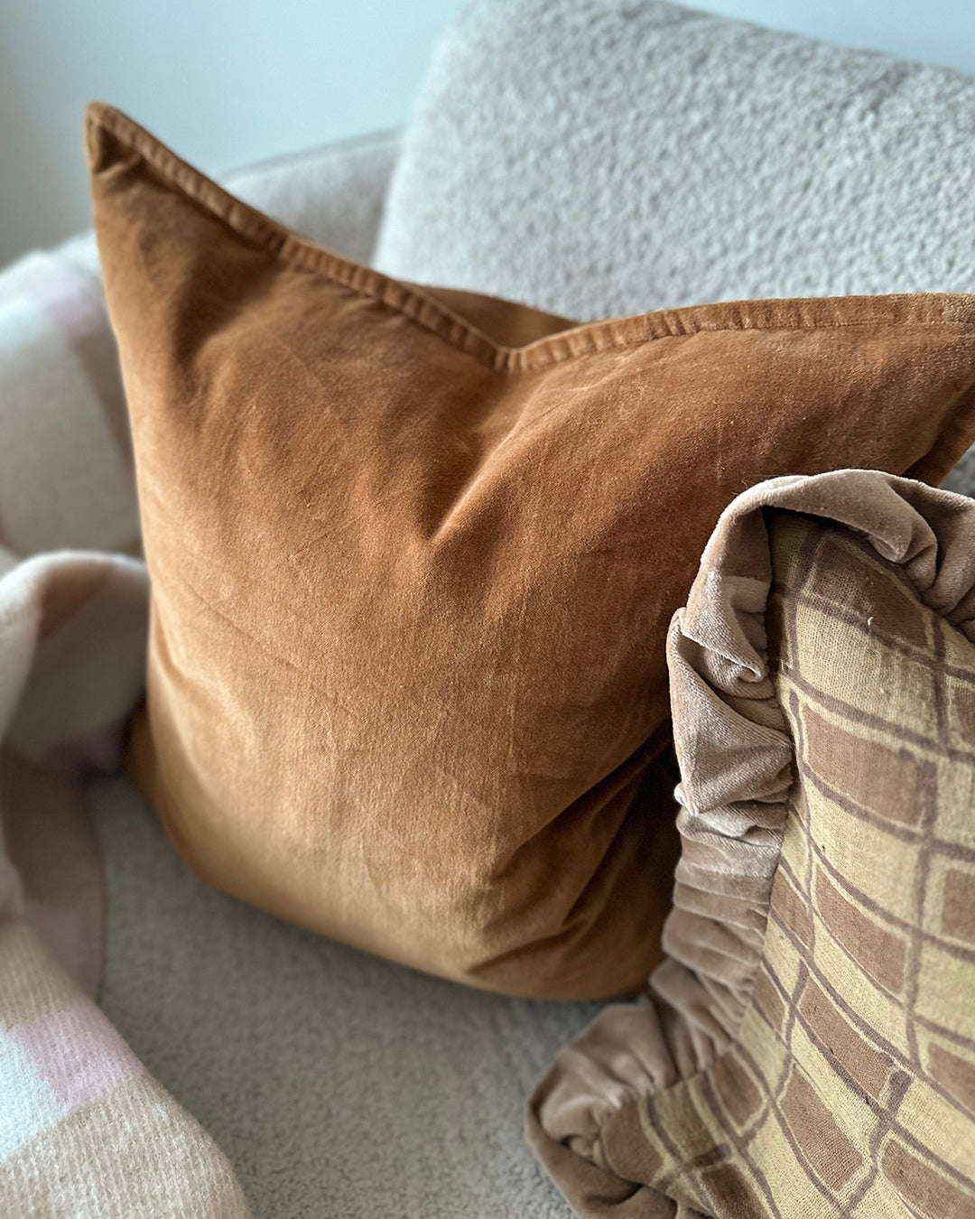 Terrakottafärgad kudde i bomullssammet, Classic Velvet, placerad i soffa tillsammans med mönstrad kudde i beige toner.