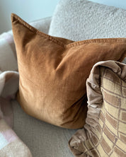 Terrakottafärgad kudde i bomullssammet, Classic Velvet, placerad i soffa tillsammans med mönstrad kudde i beige toner.