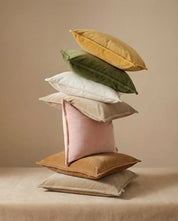 Stack of assorted multicolored velvet throw pillows in neutral, green, pink, and yellow tones.