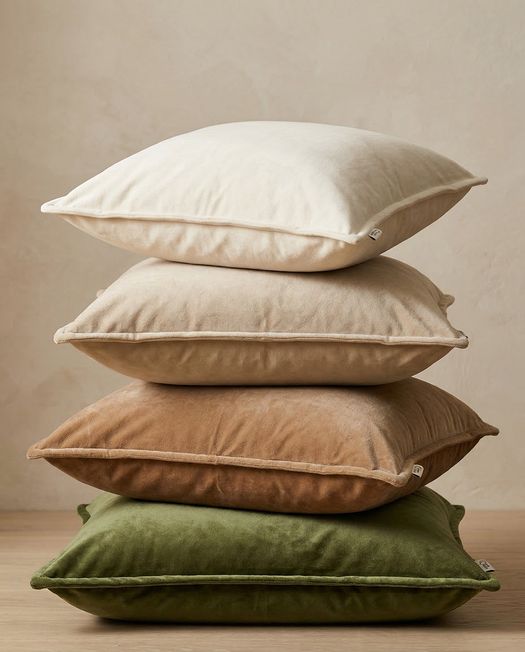 Stapel med fyra mjuka sammetskuddar i nyanser av beige, brunt och grönt.