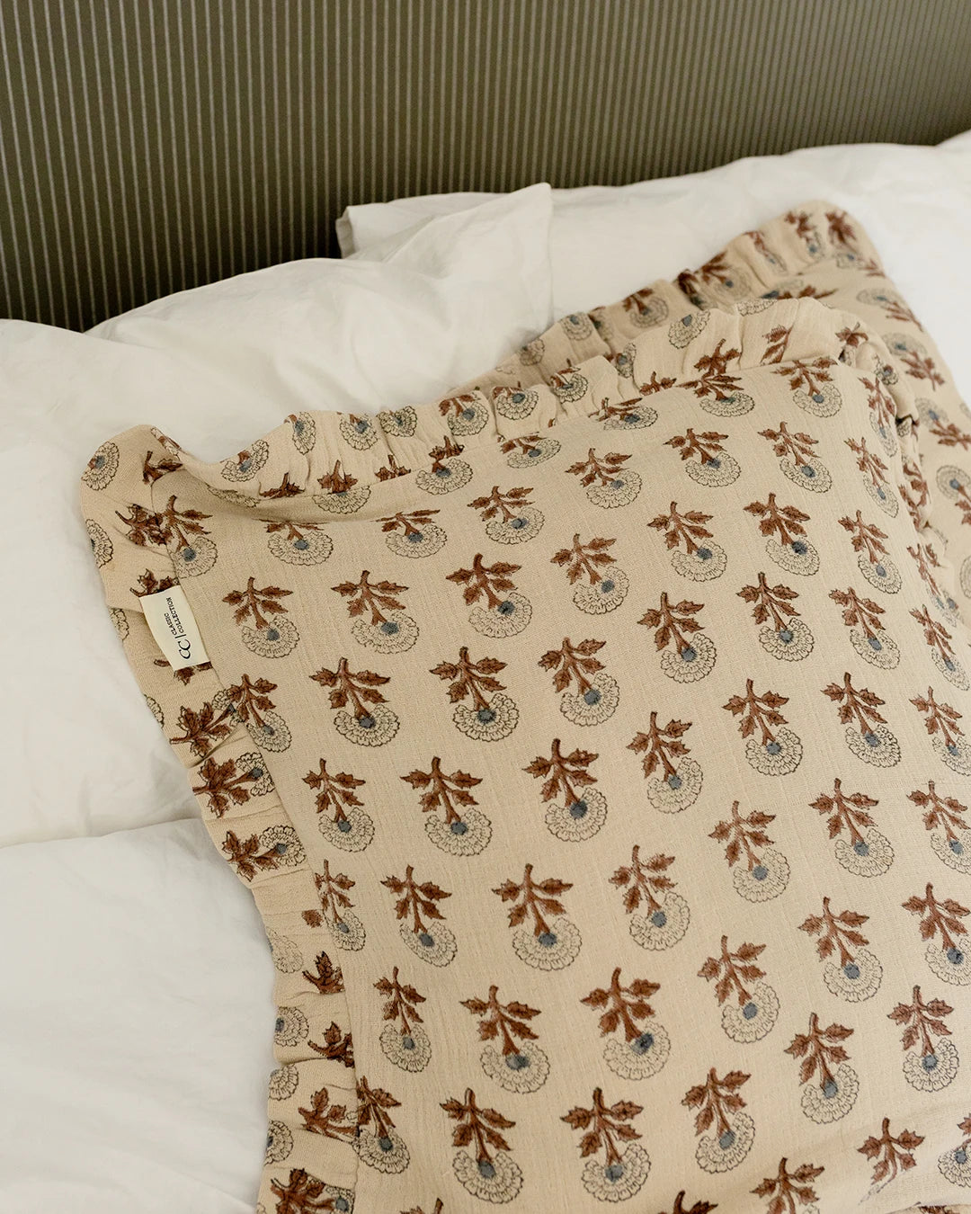 Kuddfodral Marigold Mocha i handtryckt bomull med mönster och volangkant, placerat på en bäddad säng.