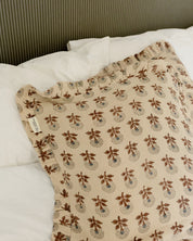 Kuddfodral Marigold Mocha i handtryckt bomull med mönster och volangkant, placerat på en bäddad säng.