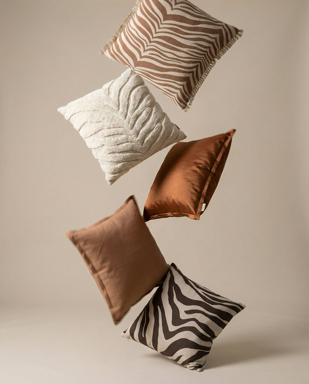 Fem prydnadskuddar i olika texturer och nyanser av beige och brunt med zebra- och växtmönster som svävar i luften.