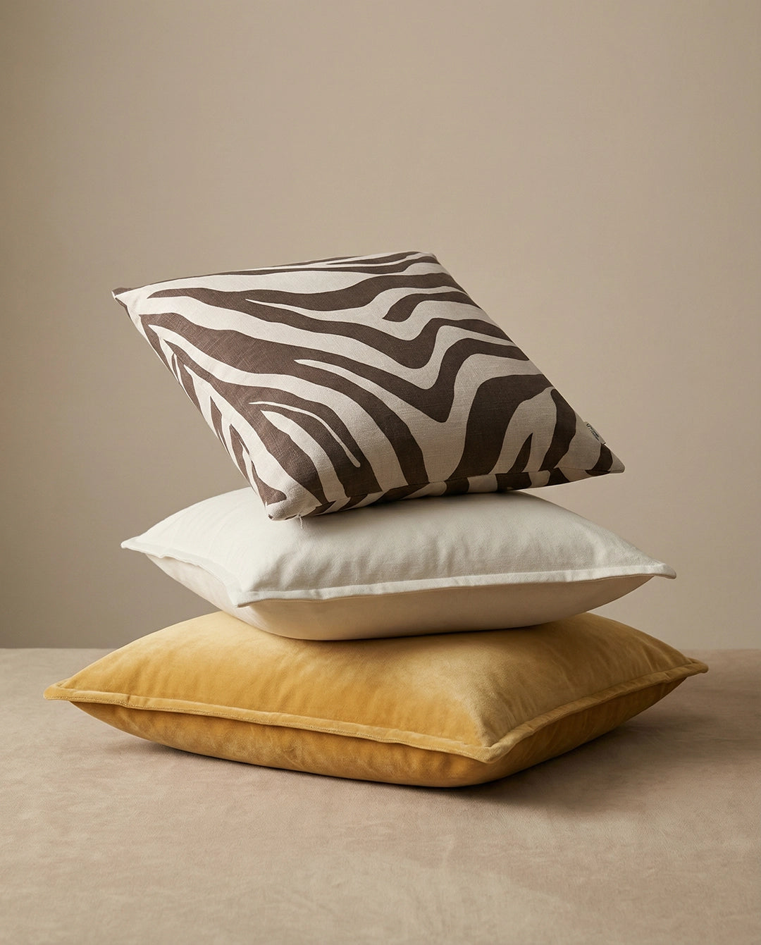 Stack of three square decorative throw pillows in zebra print, plain off-white linen, and yellow velvet texture.