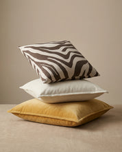 Stack of three square decorative throw pillows in zebra print, plain off-white linen, and yellow velvet texture.