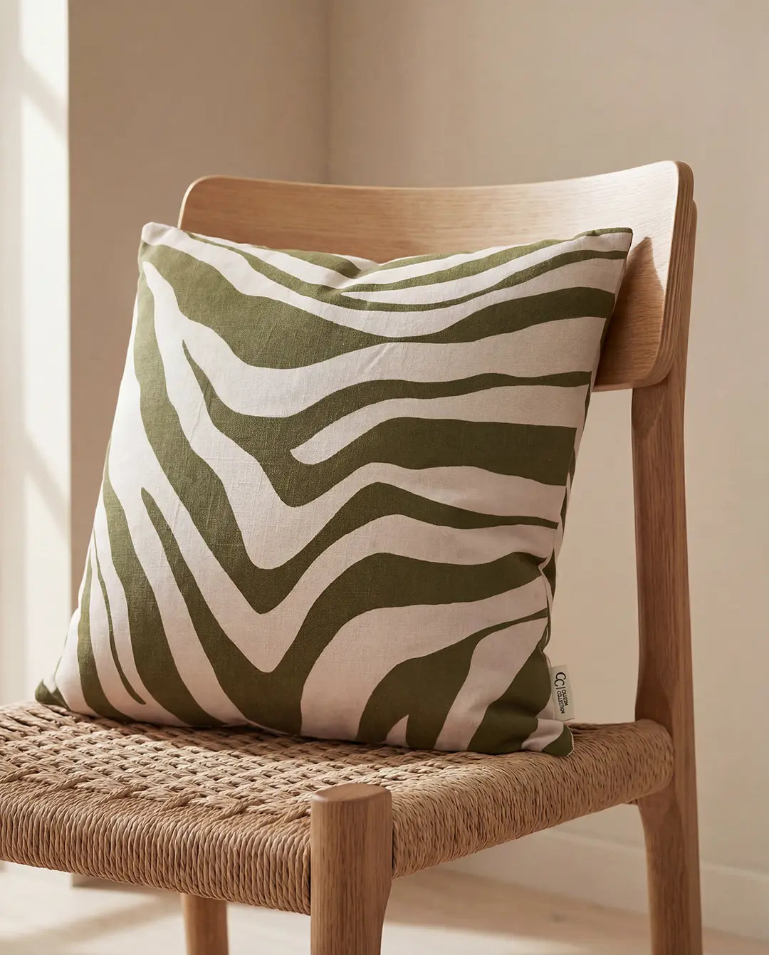 Square throw pillow with an olive green and beige zebra print pattern, resting on a wooden chair.
