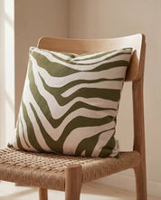 Square throw pillow with an olive green and beige zebra print pattern, resting on a wooden chair.