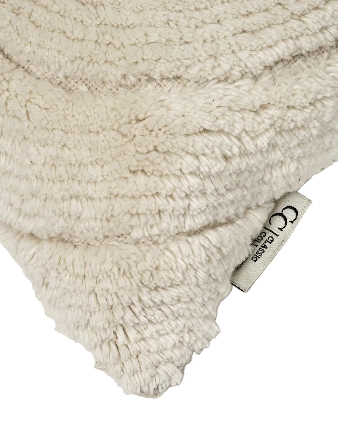 Detalj av Kudde Swirl Off-white i ull. Närbild som visar det tuftade, organiska swirlmönstret med tydlig relief, den vävda basen samt Classic Collection-etikett i sidan.