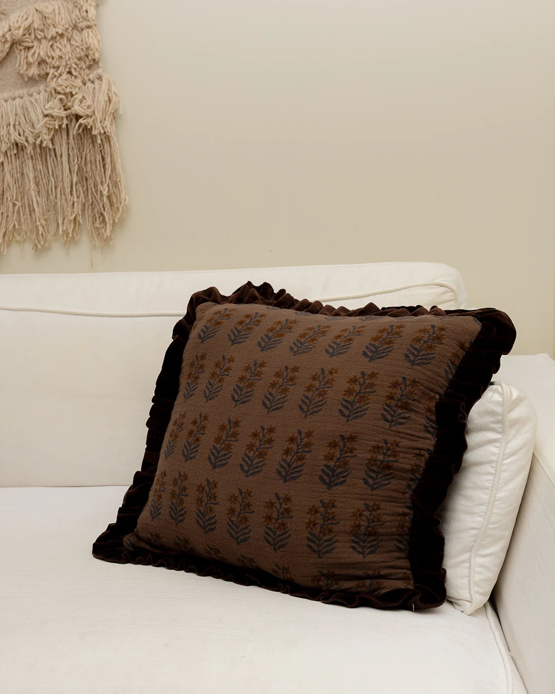 Kuddfodral Tamarind Aubergine 50x50 cm i handtryckt bomull med mönster och volangkant, placerat i en soffa i hemmiljö.