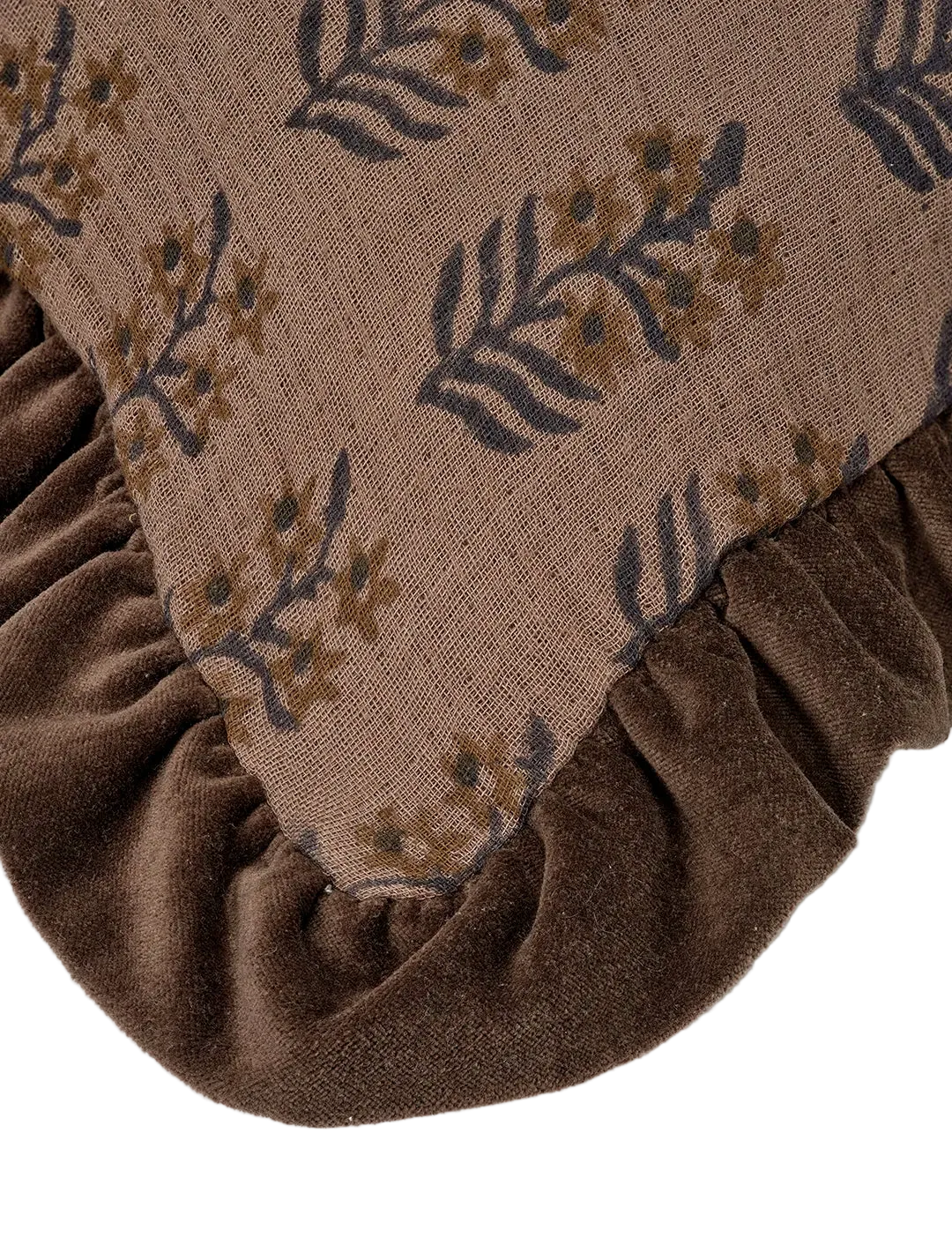 Kvadratiskt kuddfodral i bomull, 50x50 cm, med blommigt blockprintmönster i aubergine och bruna toner. Volangkant i matchande brun ton. Närbild på ett hörn på kudden.