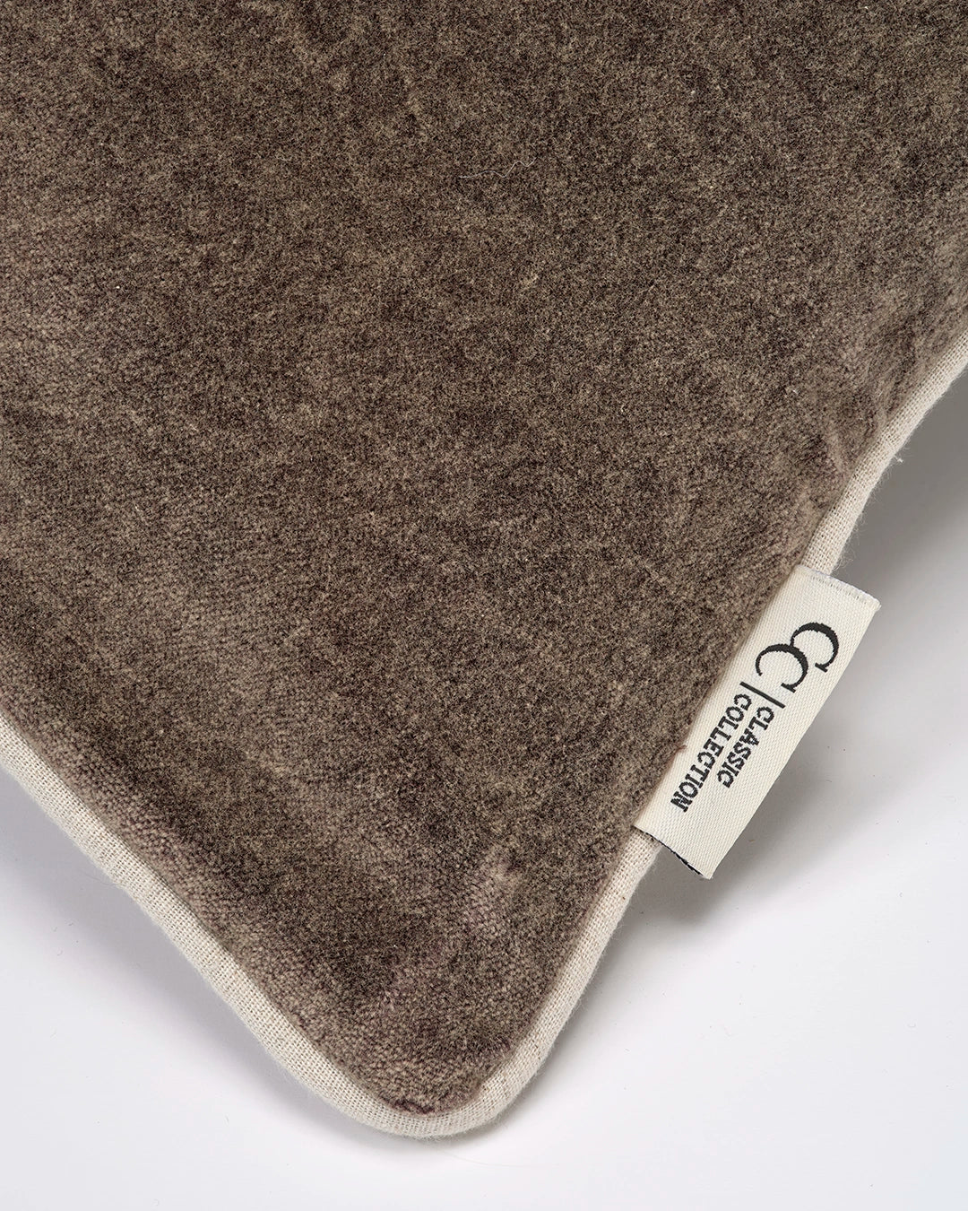Närbild av Classic Velvet kuddfodral i mörk brun bomullssammet med tvättad yta, passpoalkant och synlig Classic Collection-etikett.