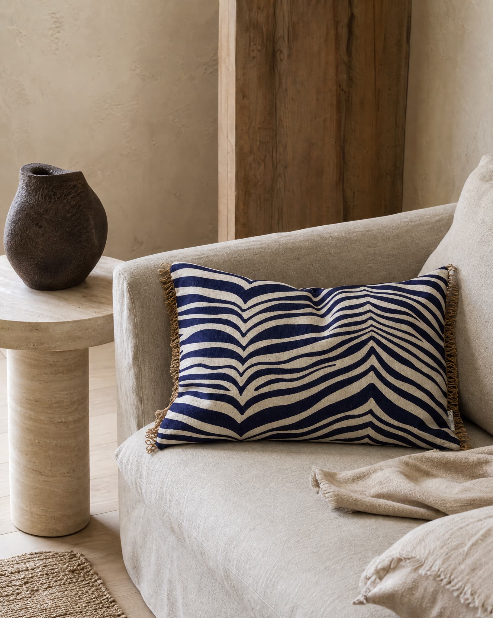Kudde Zebra Navy, 40x60 cm, med grafiskt zebramönster i mörkblått och naturvitt samt dekorativa fransar på kortsidorna, placerad i en ljus soffa i en harmonisk vardagsrumsmiljö.