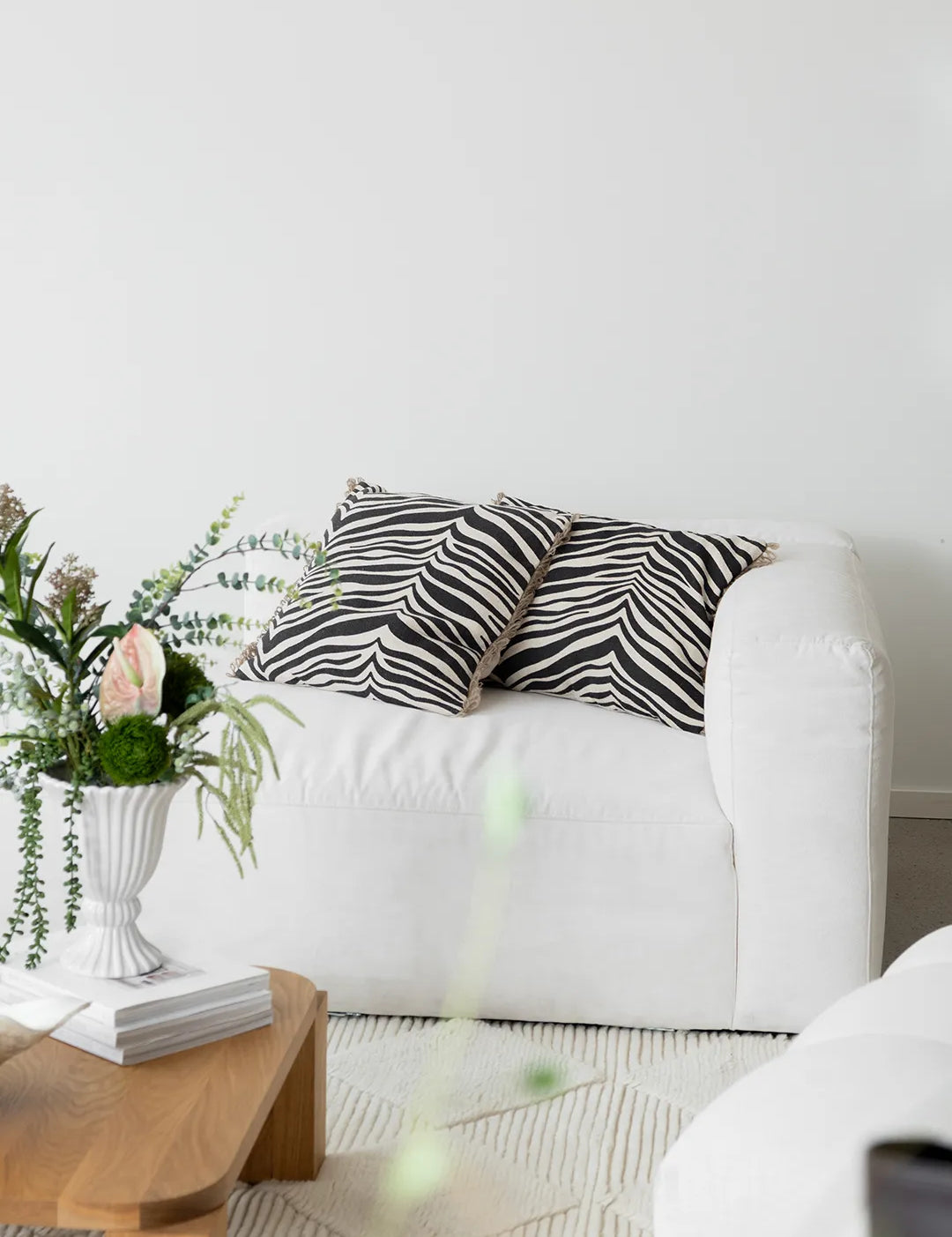 Kuddar Zebra Svart i storlekarna 50x50 cm och 40x60 cm, med handtryckt zebramönster på bomull och kant i jute, placerade på vit fåtölj.