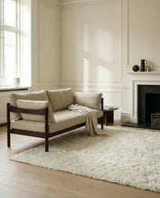 Modernes Zweisitzer-Sofa mit beigem Leinenbezug und dunklem Holzgestell in einem hellen Wohnzimmer.