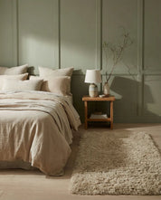 Beige linen bedding set with textured pillows and a matching plush shag rug in a sage green bedroom.